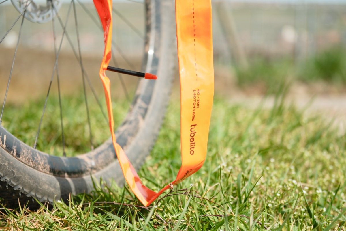 Chambre à air TPU Tubolito orange déroulée devant une roue de gravel dans l'herbe