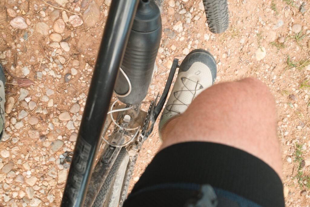 Vue du cycliste sur son genou et sa chaussure en plein coup de pédale, sur un chemin de gravier