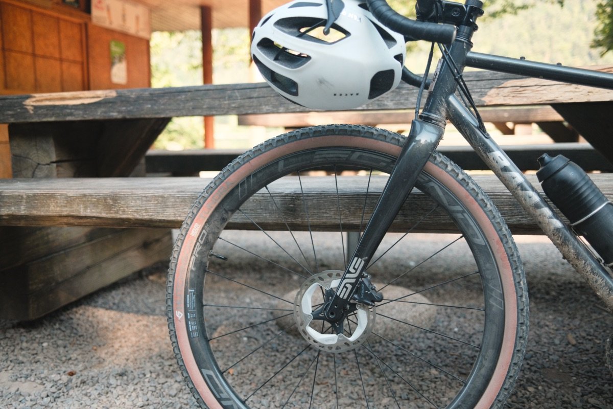 Gravel acier : ce que plus de 2 ans sur un Reynolds 853 m'ont appris 1 Avant d’un gravel acier BAAM Argh couvert de boue, avec sa fourche carbone ENVE et un casque posé sur le cintre, garé près d’une table de pique-nique.