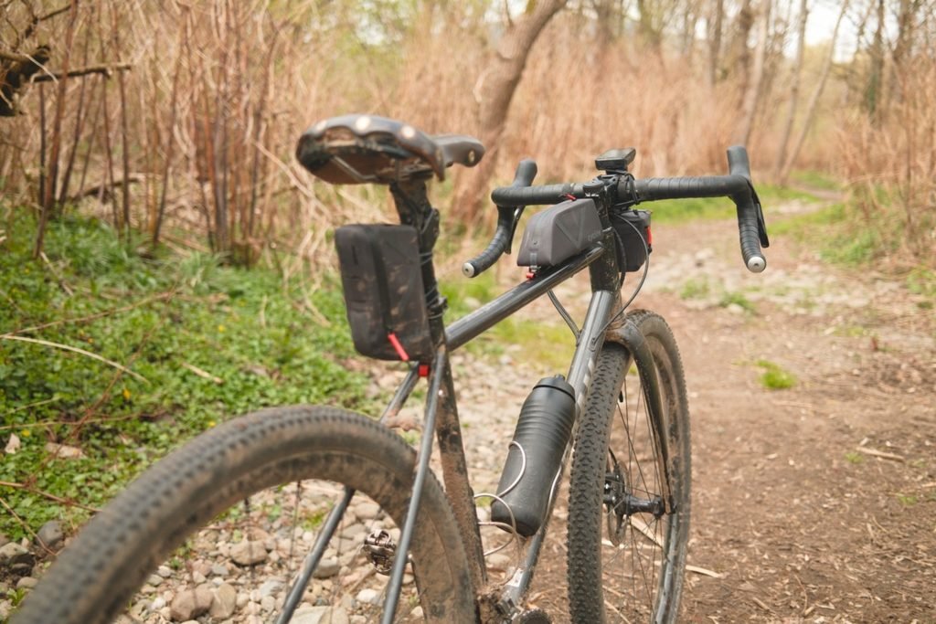 Quelle sacoche gravel pour rouler à la journée ? 6 Gravel boueux sur un chemin, équipé d’une petite top tube, d’une mini sacoche de guidon et d’une petite sacoche sous la selle