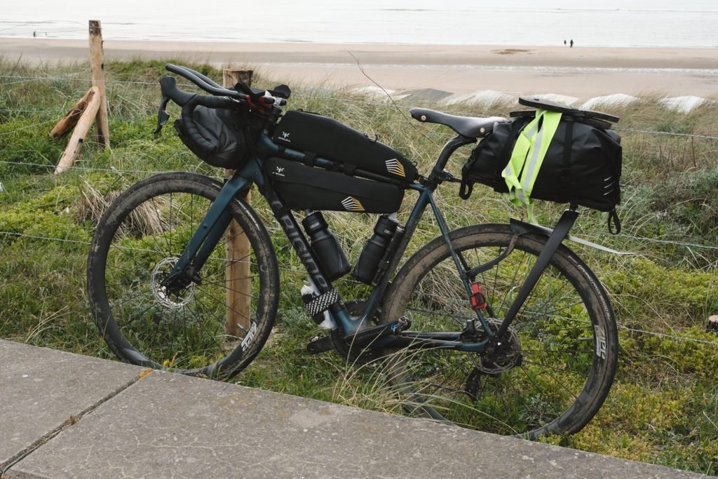 Gravel acier : ce que plus de 2 ans sur un Reynolds 853 m'ont appris 6 Vélo de route carbone Origine GTR Evo Ultra équipé de sacoches, couvert de boue au bord d’une plage pendant le Metz-Amsterdam.